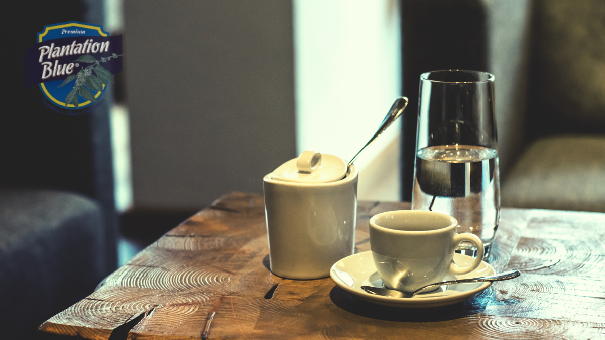 Plantation Blue coffee cup on a wooden table with a glass of water, illustrating how to measure coffee for a consistently great brew.