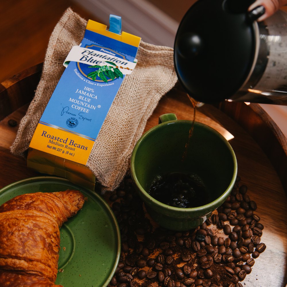 Plantation Blue Medium Roast bag beside a fresh cup of coffee being poured